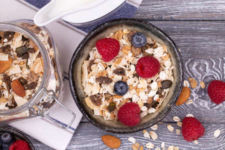 Homemade granola with nuts, raspberries and blueberries, milk on a gray whitewashed rustic table, top view, copy space. Healthy breakfastの写真素材