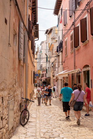 Rovinj, Croatia - June 25, 2017: Narrow cobbled street, facades of houses with wooden shutters and tourists walking in an old European city. vertical photo.のeditorial素材
