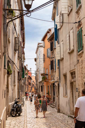 Rovinj, Croatia - June 25, 2017: Narrow cobbled street, facades of houses with wooden shutters and tourists walking in an old European city. vertical photo.のeditorial素材