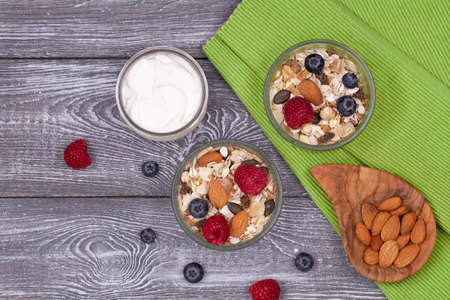 Healthy breakfast with homemade granola with almonds, raspberries and blueberries, yogurt on a wooden rustic table, flat lay.の写真素材