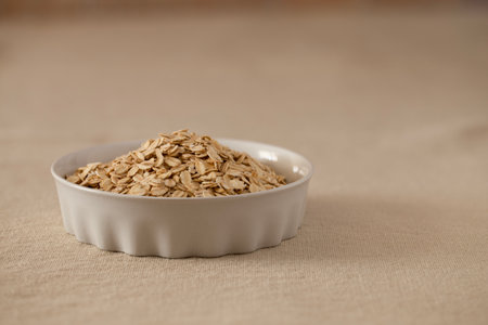 Oat flakes, cereal in a white ceramic bowl on a linen tablecloth on the table, copy space