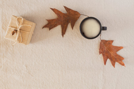 Autumn composition with a cup of coffee, autumn dry leaves, a gift wrapped in craft paper on a linen...