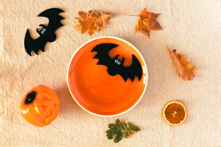 Top view of Halloween background with empty orange plate ready to place food, colorful leaves on the table and spooky carved pumpkin, black bats, flat layの写真素材