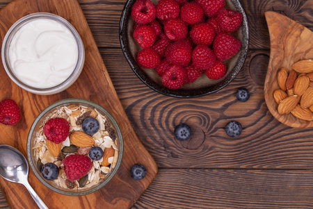 Homemade granola with nuts, raspberries and blueberries, yogurt on a wooden rustic table, top view, copy space. healthy breakfast.の写真素材
