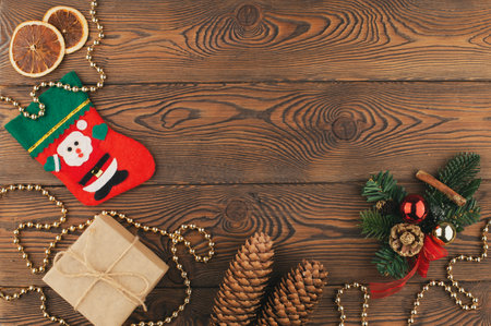 Christmas festive background with a red felt stocking with the image of Santa Claus, fir branches, cones and Christmas toys, gifts, dried oranges, on rustic wooden table. Top view, copy space.の写真素材