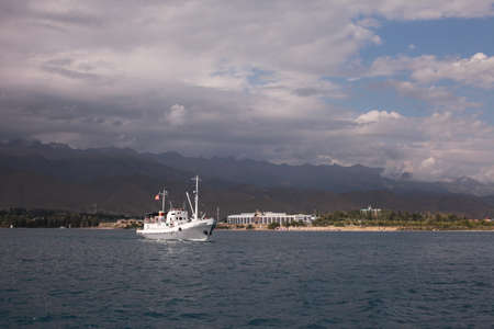 White ship departs from the coast. Mountains of Kyrgyzstan. Blue water in the ocean sea. Beautiful clouds in the sky.の写真素材