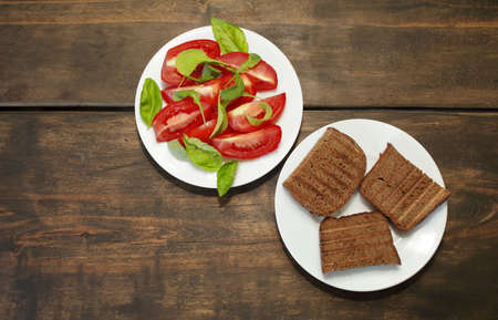 Sliced tomatoes with lettuce on a white plate. Fresh bread toast. Healthy eating concept. High quality photoの写真素材