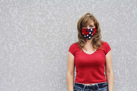 Girl in a protective mask against coronavirus on a background of a gray concrete wall. Primary red colorの写真素材