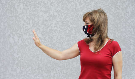 Girl in a protective mask against coronavirus on a background of a gray concrete wall. Primary red colorの写真素材