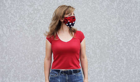 Girl in a protective mask against coronavirus on a background of a gray concrete wall. Primary red colorの写真素材