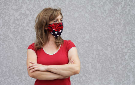 Girl in a protective mask against coronavirus on a background of a gray concrete wall. Primary red colorの写真素材