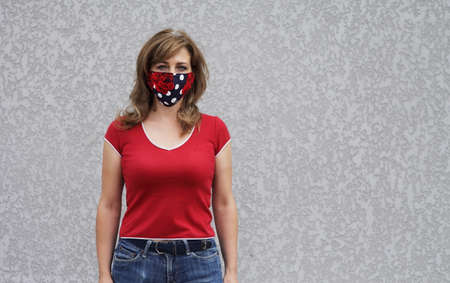 Girl in a protective mask against coronavirus on a background of a gray concrete wall. Primary red colorの写真素材