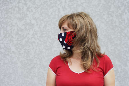 Girl in a protective mask against coronavirus on a background of a gray concrete wall. Primary red colorの写真素材