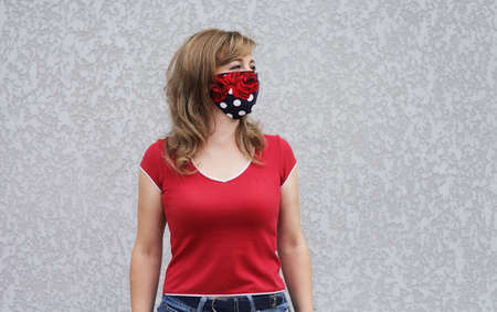 Girl in a protective mask against coronavirus on a background of a gray concrete wall. Primary red colorの写真素材