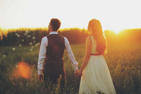 Wedding. The bride and groom hold hands and walk in the park in the sunset lightの写真素材