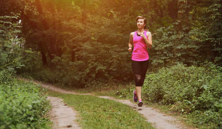 Young fitness woman running in the morning forest trail. Motivation healthy fit living. Running shoe of the person running in nature with beautiful sunlight. Woman warming up before runningの写真素材
