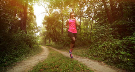 Young fitness woman running in the morning forest trail. Motivation healthy fit living. Running shoe of the person running in nature with beautiful sunlight. Woman warming up before runningの写真素材