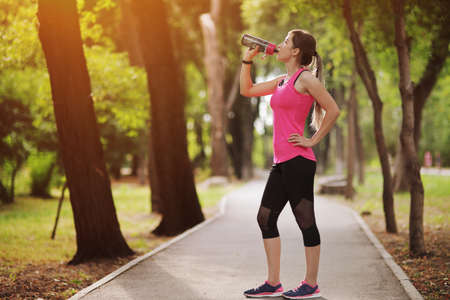 Beautiful fitness athlete runner woman drinking water in the park. Water bottleの写真素材
