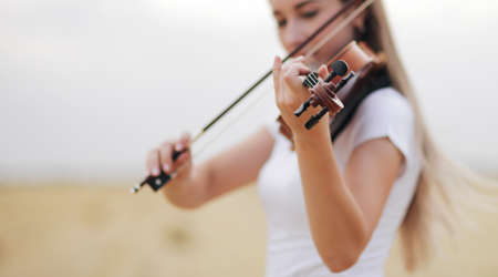 Beautiful romantic girl with loose hair playing the violin in the field after the harvest. Square sheaves of hay in the field. Violin trainingの写真素材