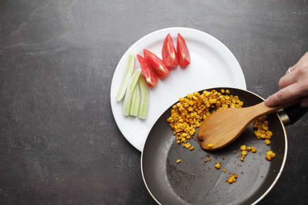 Diet. Organic Grilled Corn in a frying pan. Organic farm vegetables. Chopped tomato and cucumber on a white plate. Wooden spoon in hand. Environmentally friendly productsの写真素材