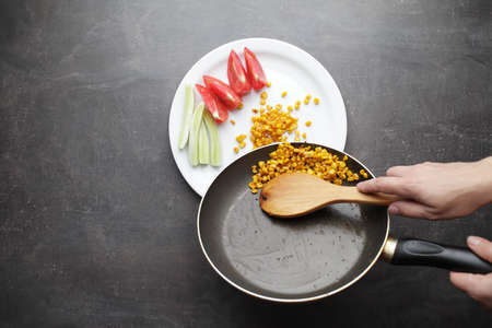 Diet. Organic Grilled Corn in a frying pan. Organic farm vegetables. Chopped tomato and cucumber on a white plate. Wooden spoon in hand. Environmentally friendly productsの写真素材
