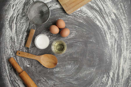 Chicken egg, flour, olive oil, milk, kitchen tool on gray table background. Products for baking bakery products. Cutting board, rolling pin, flour sieve, wooden spoon. For bread or cakeの写真素材
