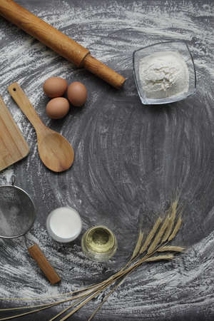 Chicken egg, flour, olive oil, milk, wheat ears, kitchen tool on gray table background. Products for...