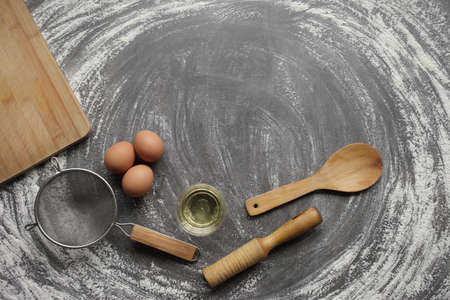 Chicken egg, flour, olive oil, kitchen tool on gray table background. Products for baking bakery products. Cutting board, rolling pin, flour sieve, wooden spoon. For bread or cakeの写真素材