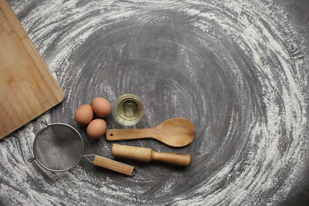 Chicken egg, flour, olive oil, kitchen tool on gray table background. Products for baking bakery products. Cutting board, rolling pin, flour sieve, wooden spoon. For bread or cakeの写真素材