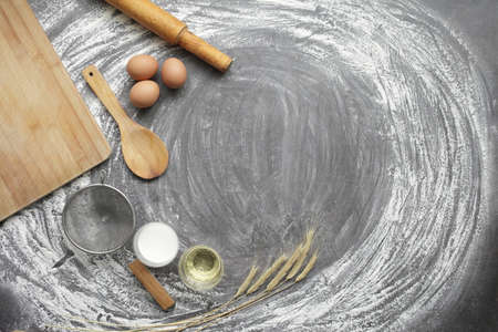 Chicken egg, flour, olive oil, milk, wheat ears, kitchen tool on gray table background. Products for baking bakery products. Cutting board, rolling pin, flour sieve, wooden spoon. For bread or cakeの写真素材