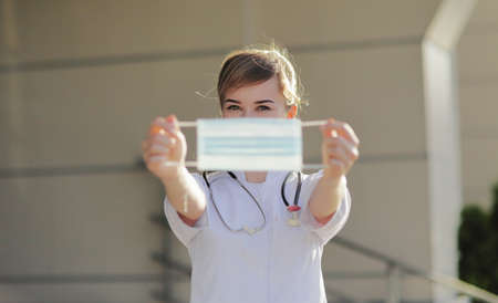 Young woman doctor or nurse showing medical face mask close up. Prevention Covid-19 healthcare concept. Stethoscope over the neck. Female, girl.の写真素材