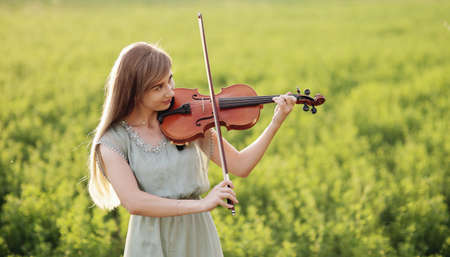 Romantic woman with loose hair playing the violin. Sunset light in nature. Violin trainingの写真素材