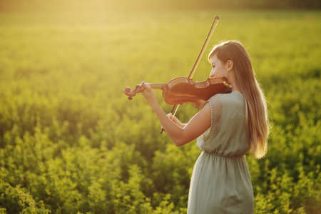 Romantic woman with loose hair playing the violin. Sunset light in nature. Violin trainingの写真素材