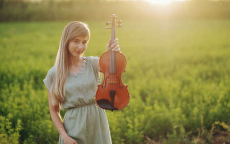 Female musician violinist holding a violin in her hands in sunset light. Violin training conceptの写真素材