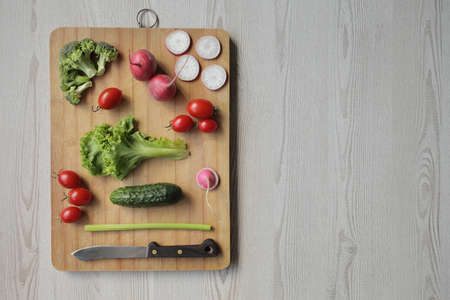 Fresh vegetables on a cutting board on a light wooden table Tomatoes, cucumber, lettuce, broccoli, radish, knifeの写真素材