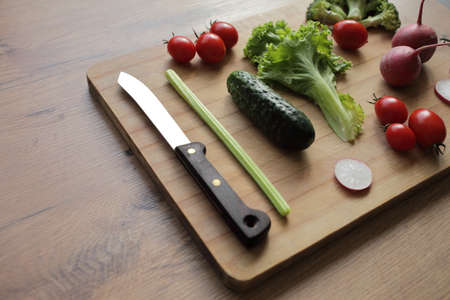 Fresh vegetables on a cutting board on a wooden table Tomatoes, cucumber, lettuce, broccoli, radish,...