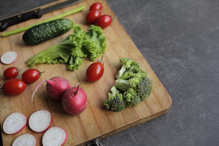Fresh vegetables on a cutting board on a gray table Tomatoes, lettuce, broccoli, radishの写真素材