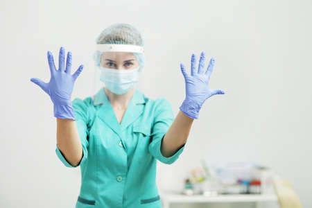 Female doctor or nurse in uniform, medical mask, face shield shows hands in gloves. Coronavirus...