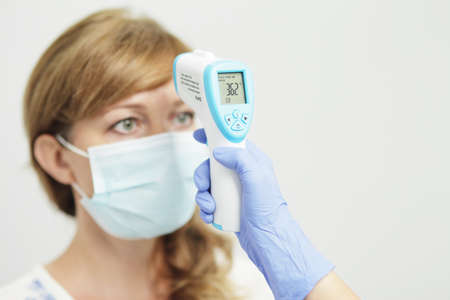 Medical woman in uniform measures the temperature of a woman with a pyrometerの写真素材