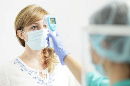 Medical woman in uniform measures the temperature of a woman with a pyrometerの写真素材