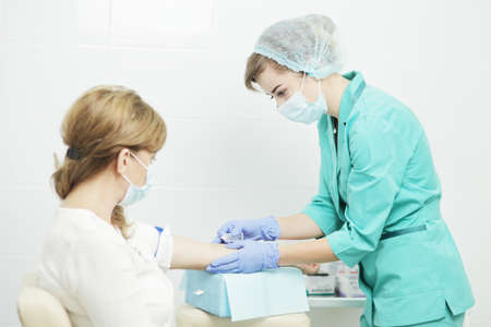A female nurse in a medical mask takes a blood sample from the patient.の写真素材