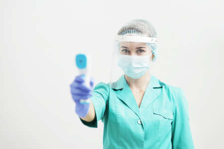 Female doctor or nurse in protective mask at hospital holds pyrometer in hand. Safety measures...