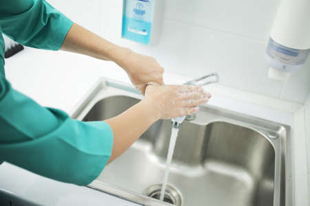 A woman doctor in a protective mask and medical uniform washes her hands thoroughly in the hospital....