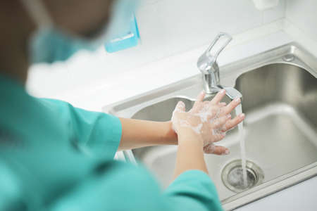 A woman doctor in a protective mask and medical uniform washes her hands thoroughly in the hospital....