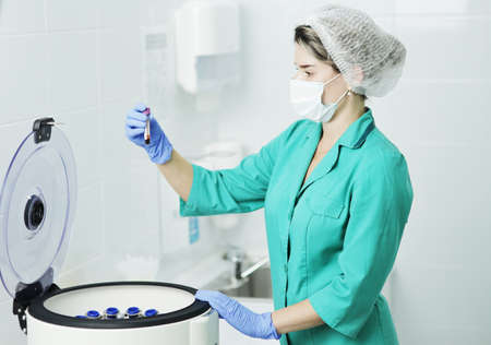 A woman nurse or doctor in a medical mask holds a test tube for a blood test. laboratory centrifuge for the separation of blood componentsの写真素材