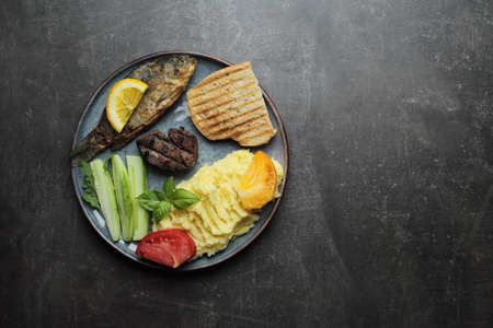 Fried fish, meat steak and vegetables on a plate. Concrete gray countertop. High quality photoの写真素材