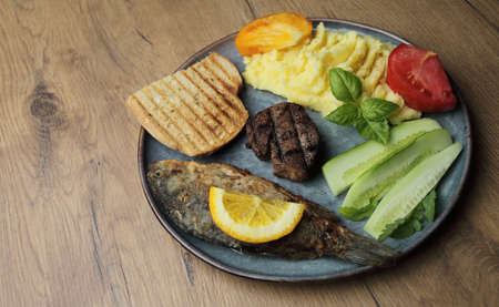 Fried fish, meat steak and vegetables on a plate. On a wooden table. High quality photoの写真素材