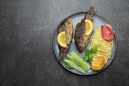 Fried fish and vegetables on a plate. Concrete gray countertop. High quality photoの写真素材