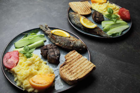 Fried fish, meat steak and vegetables on a plate. Concrete gray countertop. High quality photoの写真素材