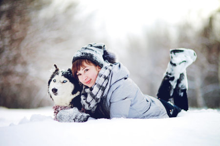 Girl lies in the snow with a siberian husky dog in the winter forestの写真素材